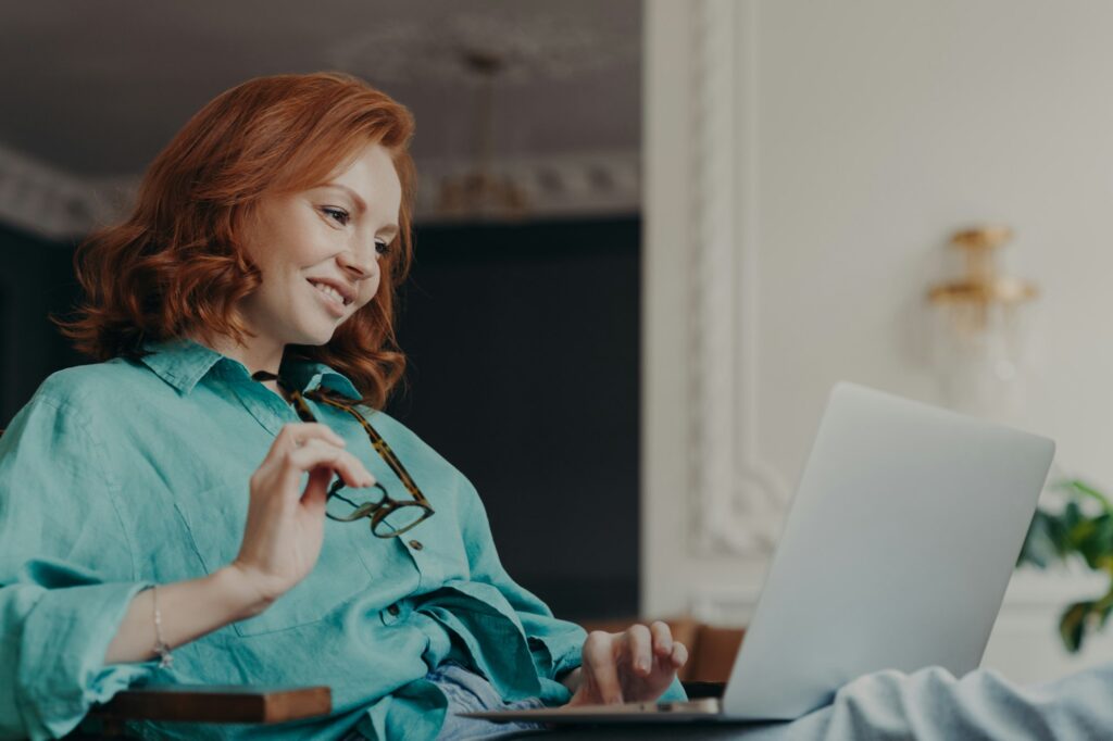 Side view of pretty redhead woman concentrated on remote job, prepares publication for web page